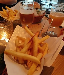 Baskets of fries on a tables with a couple glasses of craft beer, as well as a candle and a hamburger. 