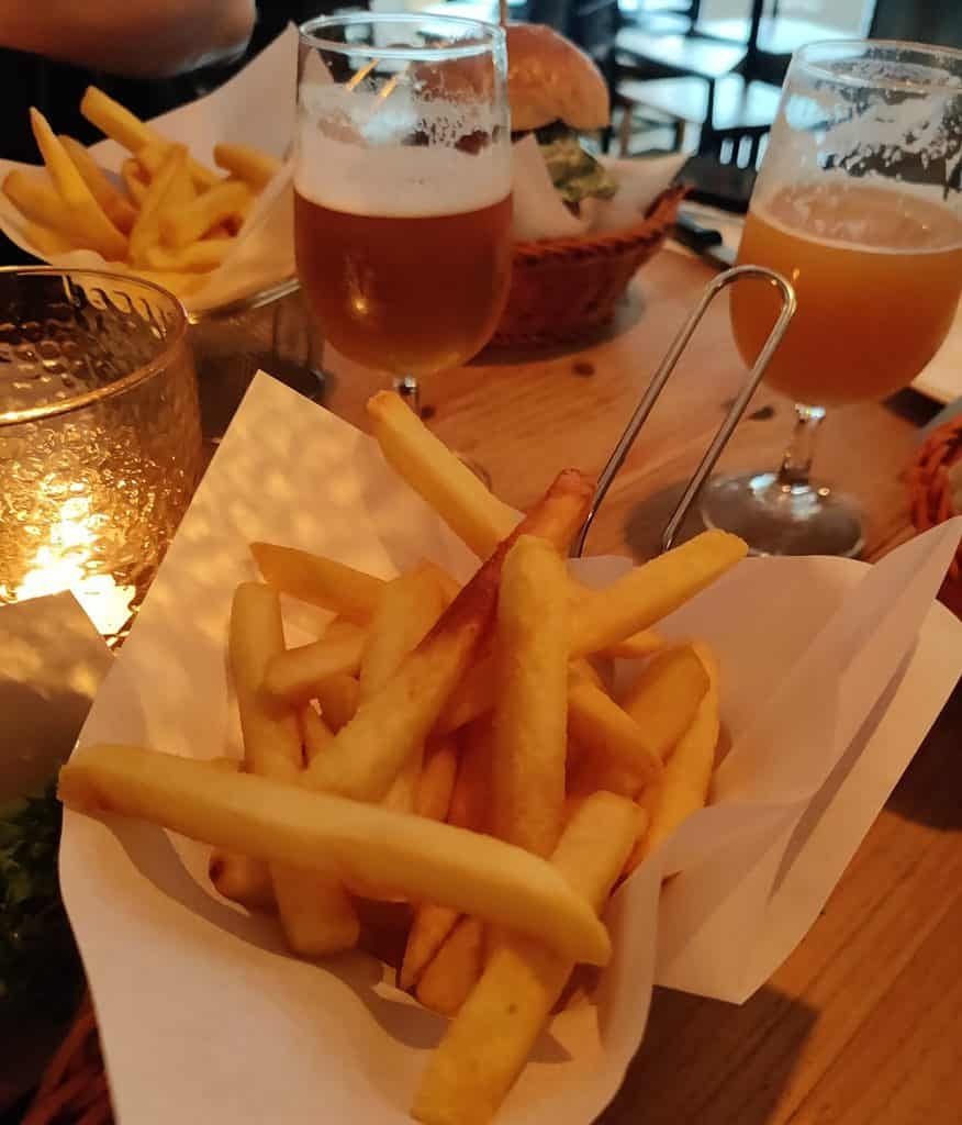 Baskets of fries on a tables with a couple glasses of craft beer, as well as a candle and a hamburger. 