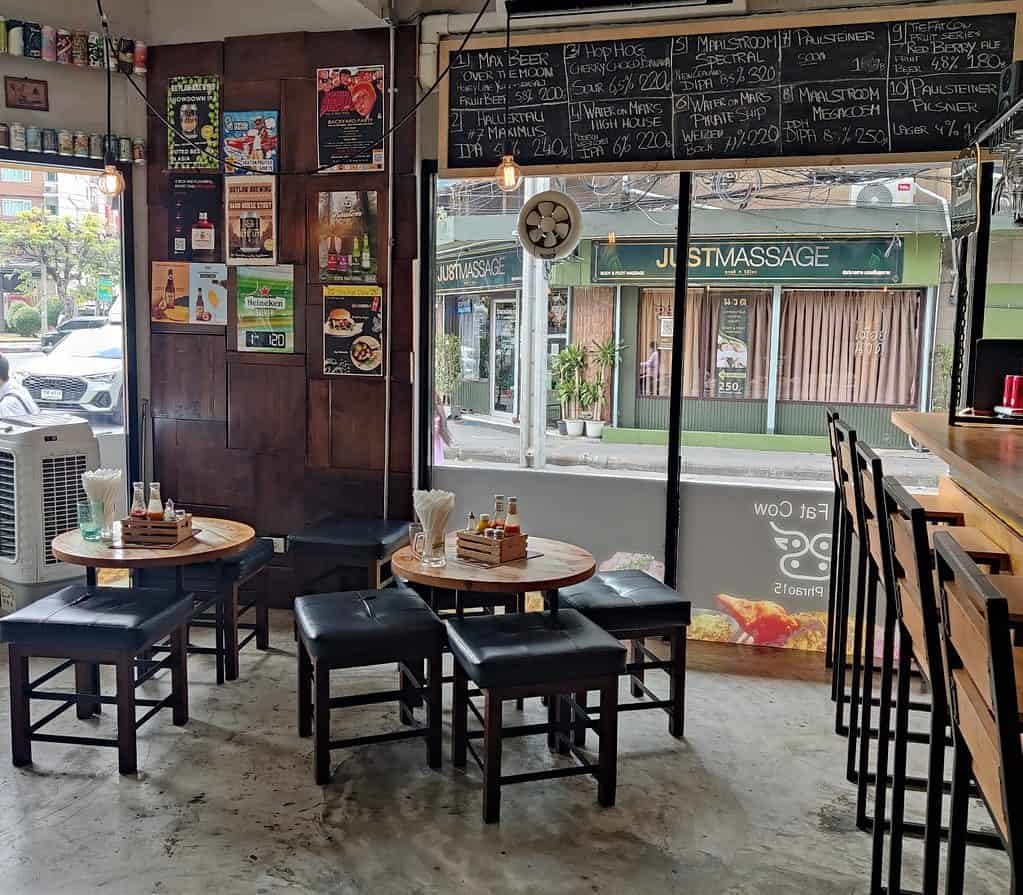 Seating and craft beer signage at the Fat Cow in Bangkok. Stools around 2 tables, and beer posters on the wall. Chalk board sign for craft beer on tap. 