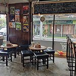 Seating and craft beer signage at the Fat Cow in Bangkok. Stools around 2 tables, and beer posters on the wall. Chalk board sign for craft beer on tap. 