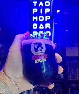 Glass of black IPA in front of Taopiphop's neon sign in Bangkok