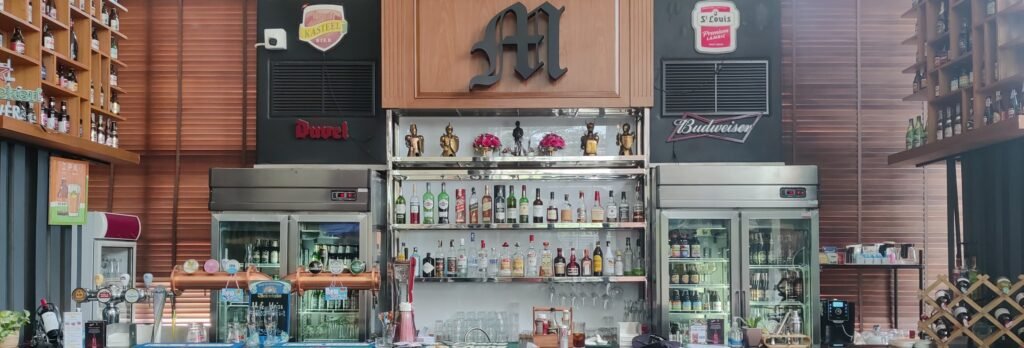 M Pub bar with beer fridges and Old fashioned M logo above the bottles of alcohol