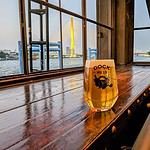 Glass of beer on a wooden table with water in the background and the sunset on a bridge. At Sheepshank Public house or Dock No. 13 in Bangkok Thailand.