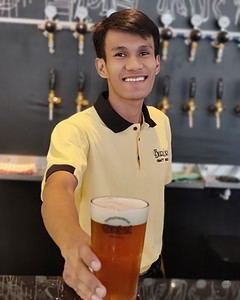 staff in a yellow shirt serving a glass of beer in a Burbrit branded glass in Bangkok Thailand