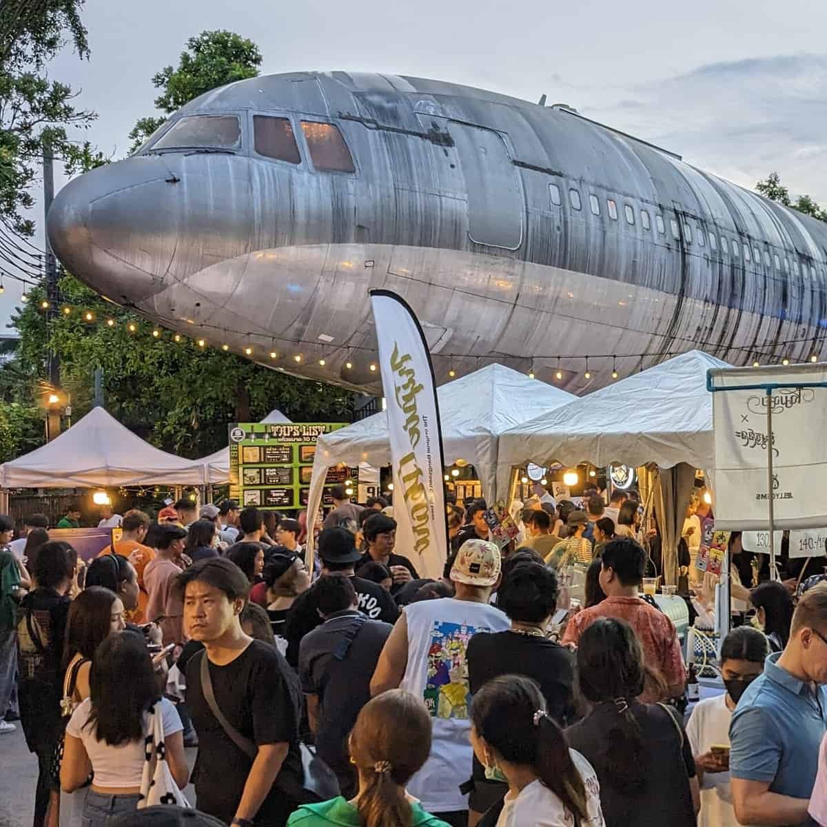 Beer Market 2 by ประชาชนเบียร์ (Beer People) at Chang Chui Creative Park in Bangkok. Large airplane above the brewery tents and beer drinking crowd in Thailand's capital.