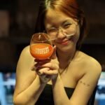Bar staff smiling in glasses serving craft beer in DOGFEST branded glass at Hair of the Dog craft beer bar in Bangkok Thailand.